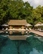 The Datai Langkawi featuring a luxurious infinity-style swimming pool surrounded by lush rainforest, elegant sun loungers, tropical landscaping, and a traditional thatched pavilion in a tranquil nature retreat.