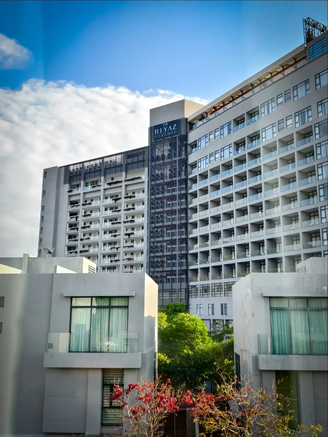 The RIYAZ Lavanya Langkawi featuring a contemporary luxury hotel with modern high-rise architecture, stylish private villas in the foreground, and elegant accommodations in the heart of Pantai Cenang.