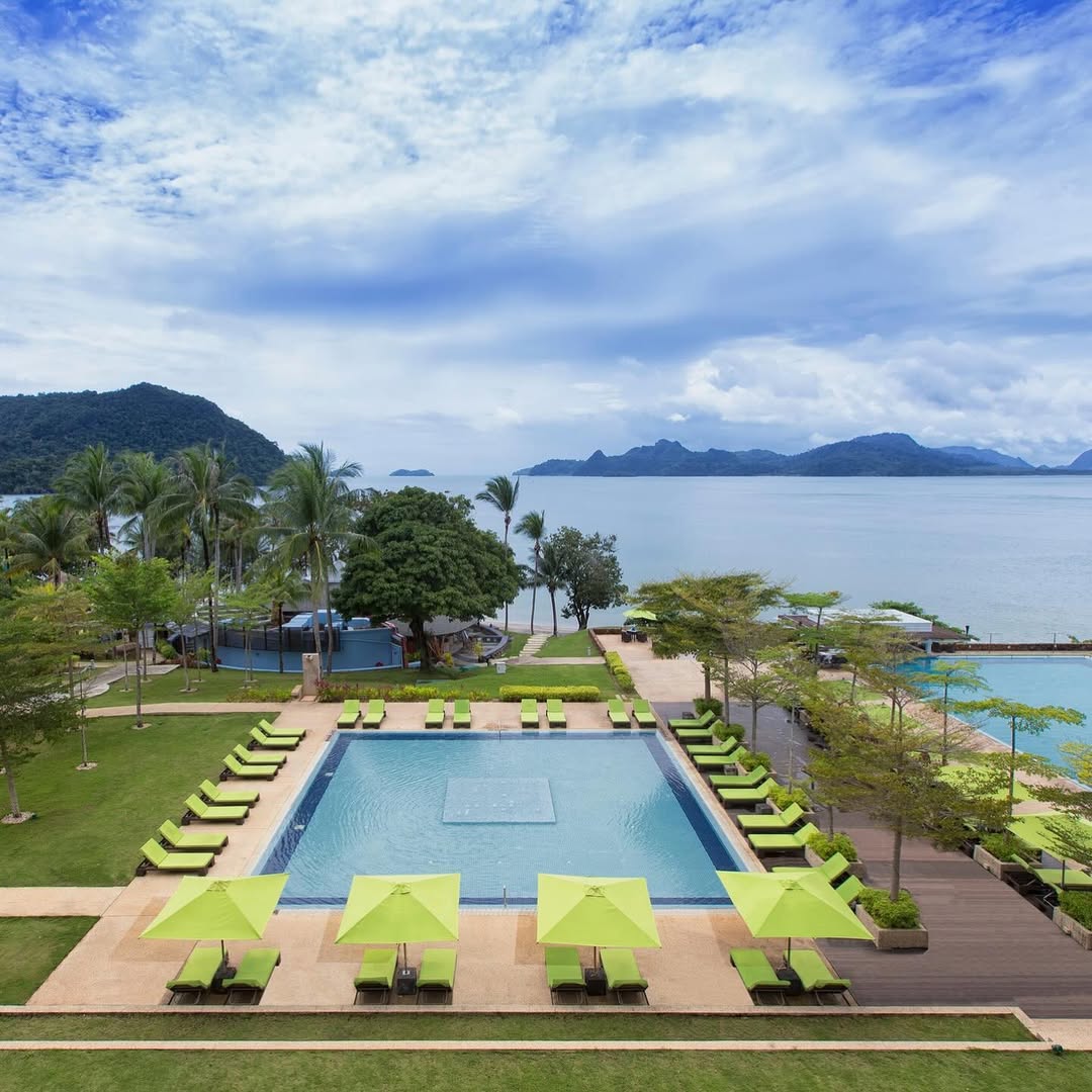 Infinity pool at The Westin Langkawi with green sun loungers, overlooking the calm sea and distant islands under a cloudy sky.