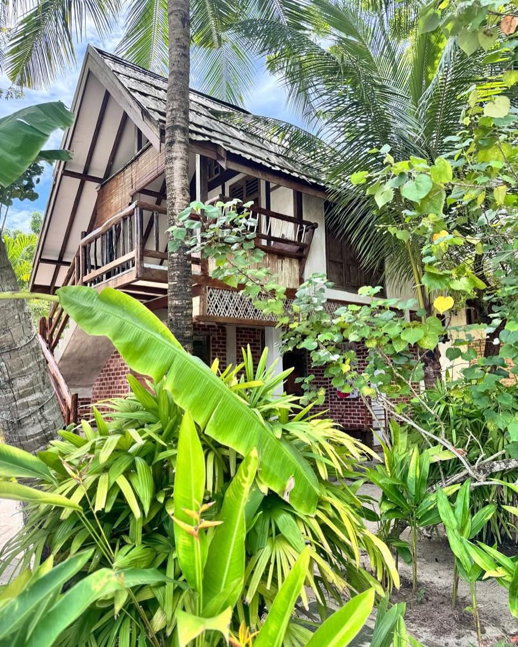 Charming tropical wooden house with a balcony, surrounded by lush greenery and palm trees at Panji Panji Tropical Wooden Homes in Langkawi.