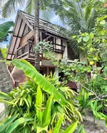 Charming tropical wooden house with a balcony, surrounded by lush greenery and palm trees at Panji Panji Tropical Wooden Homes in Langkawi.