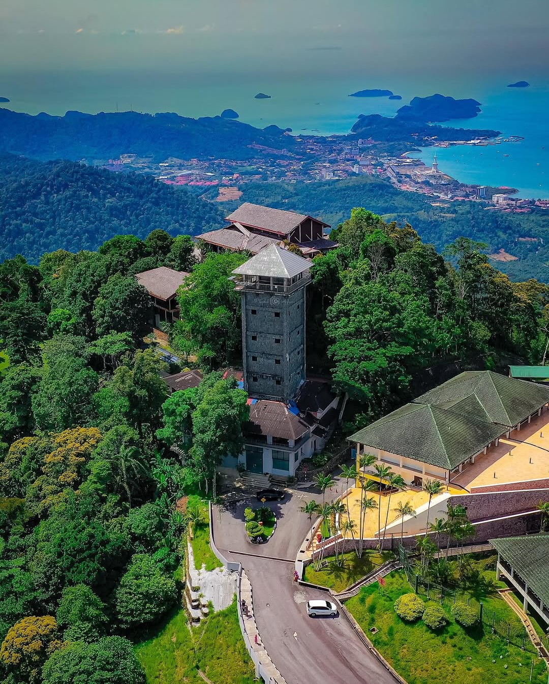 Aerial view from Gunung Raya Langkawi showing lush rainforest, hilltop buildings, and panoramic views of Kuah town and the sea.