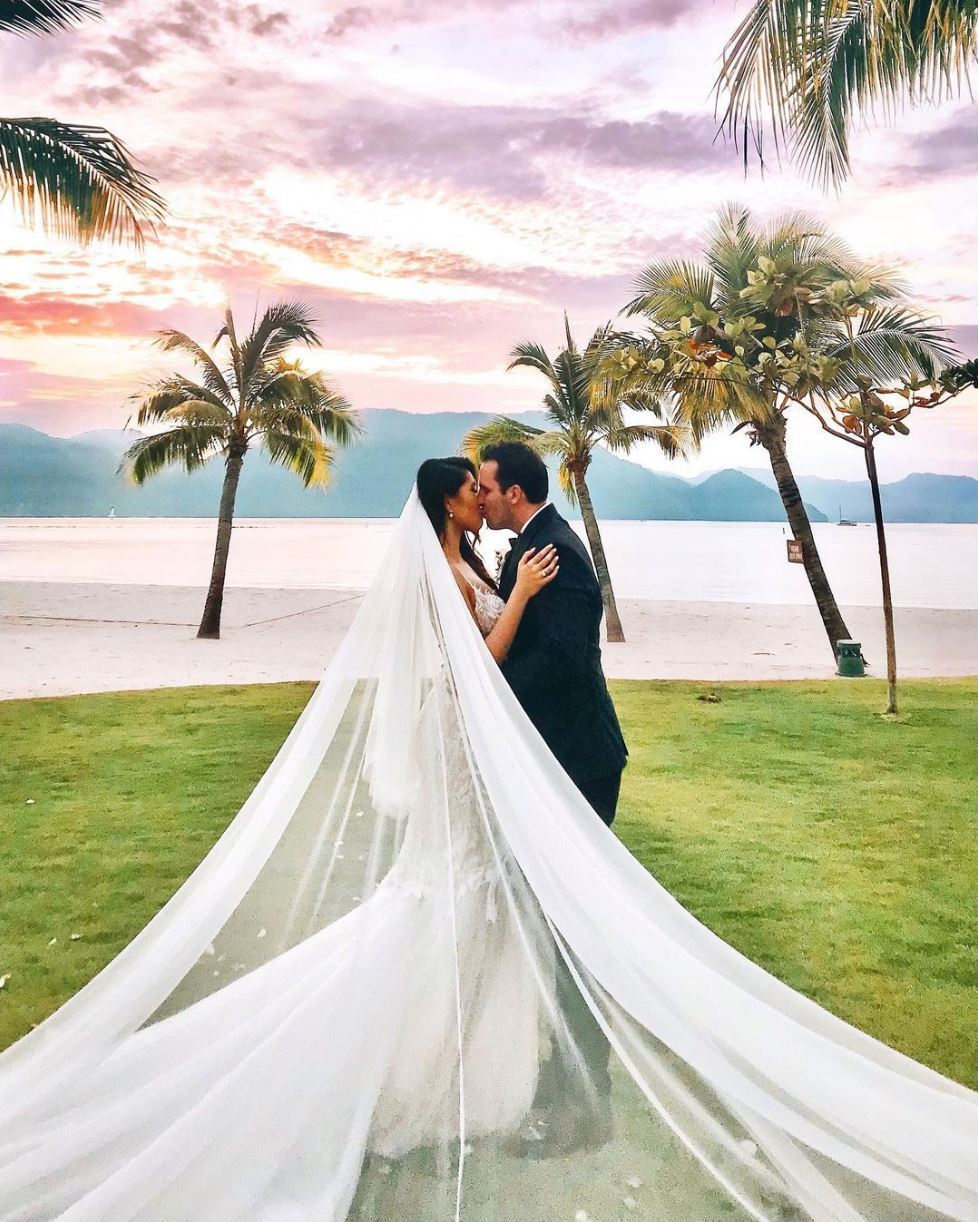Bride and groom sharing a kiss at The St. Regis Langkawi with palm trees, beach, and sunset sky in the background.