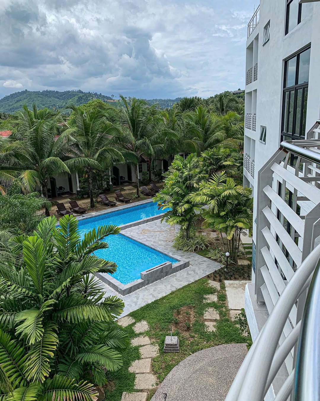 White Lodge Chalet Langkawi featuring a modern hotel overlooking a tropical swimming pool, lush palm gardens, and scenic hillside views, creating a peaceful resort retreat surrounded by nature.